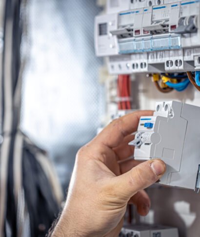 A male electrician works in a switchboard with an electrical connecting cable. Male electrician at the checkout counter on a blurred background of a switchboard.